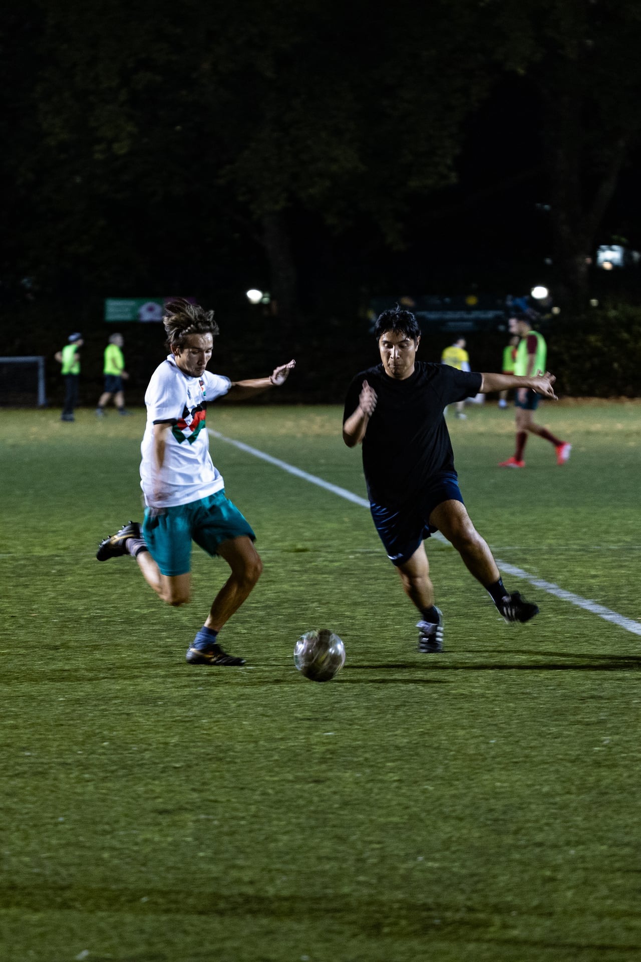 Two footballers competing for the ball during an evening session